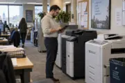 IT staff member reviewing a workplace printer fleet on a tablet in an administrative office